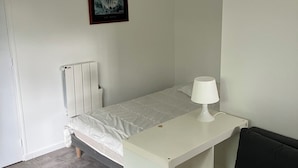 Una cama individual con colchón blanco y una mesita de noche pequeña con lámpara.