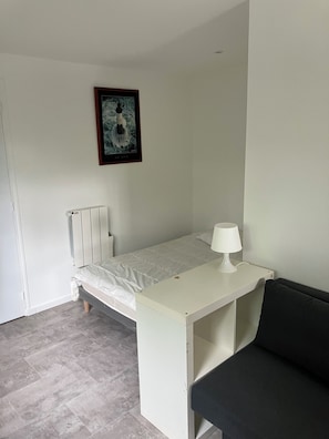 A single bed with a white mattress and a small bedside table with a lamp. - BRAND-NEW, FULLY EQUIPPED STUDIO IDEALLY LOCATED NEAR LA TORCHE (Plomeur)