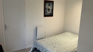 Un dormitorio con cama, radiador, puerta y un cuadro enmarcado en la pared.
