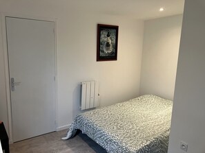 A bedroom with a bed, a radiator, a door, and a framed picture on the wall. - BRAND-NEW, FULLY EQUIPPED STUDIO IDEALLY LOCATED NEAR LA TORCHE (Plomeur)