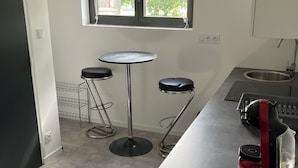 Una cocina con ventana, dos taburetes, una mesa pequeña y un electrodoméstico rojo.