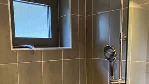 Una ducha con cabezal de ducha manual, cerramiento de vidrio y una ventana sobre la ducha.