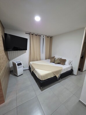 Een slaapkamer met een bed, een aan de muur bevestigde televisie, een airconditioner en een raam met gordijnen.