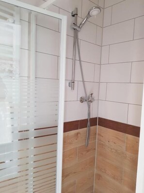 Une douche avec une porte en verre, des murs carrelés et un plancher en bois.