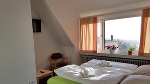 A hotel room with a bed, a chair, a small table, a window with curtains, and a radiator. - Berghotel (Bad Oeynhausen)