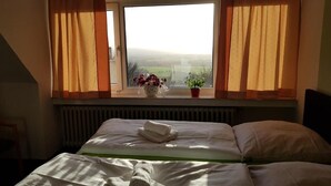 A hotel room with a bed, a window with curtains, a radiator, and a view of the countryside. - Berghotel (Bad Oeynhausen)