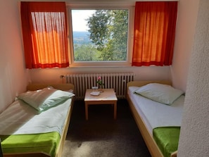 Ein kleines Zimmer mit zwei Einzelbetten, einem Tisch mit einer Vase und einem Fenster mit Vorhängen.