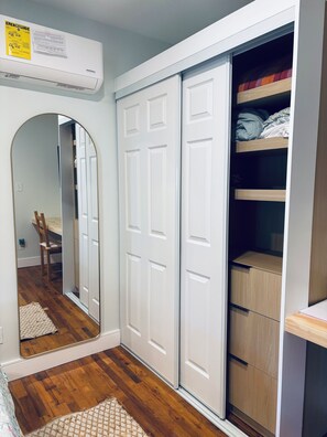Ein Zimmer mit weißem Kleiderschrank, Spiegel, Holzboden und kleinem Teppich.