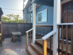 Um deck de madeira com mesa e cadeiras, uma escadaria de madeira e uma casa azul com porta marrom.