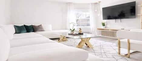 A modern living room with a white sofa, a coffee table, and a flat-screen TV mounted on the wall.