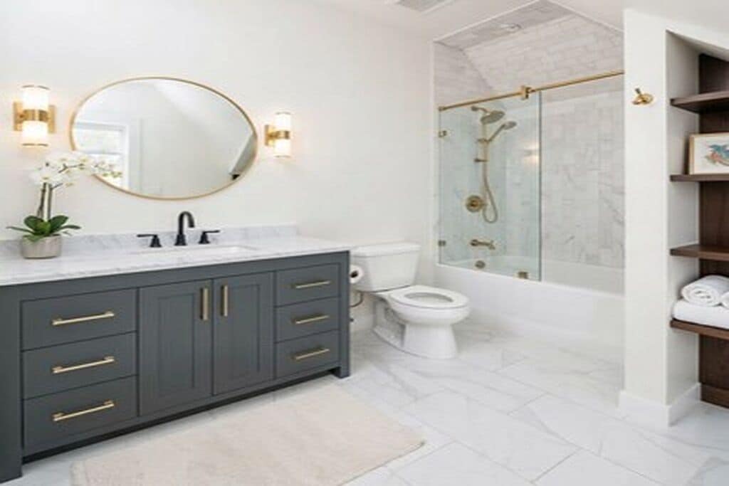 A bathroom with a dark gray vanity, a round mirror, a white toilet, and a glass-enclosed shower.