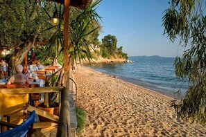 Un restaurante frente a la playa con terraza, con vistas a una playa de arena y un mar tranquilo.