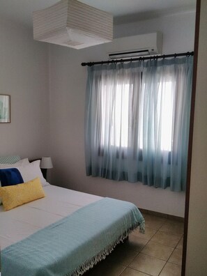 Un dormitorio con una cama, una ventana con cortinas translúcidas, un ventilador de techo y un aire acondicionado de pared.