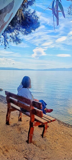 A person sitting on a wooden bench by a body of water, with a clear sky above. - Orsiida Seaside Cottage<br>K.Gatzea (Kato Gatzea)