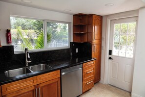 A kitchen with a black countertop, stainless steel sink, wooden cabinets, and a dishwasher.