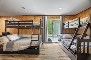 Quarto com beliche, paredes de madeira, uma janela e porta que dá para o exterior.