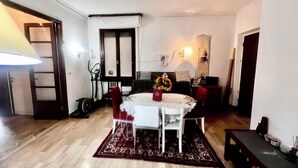 A room with a dining table, chairs, a red rug, a treadmill, and a bed with a headboard.