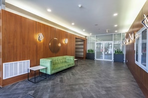 Un hall d’entrée avec un canapé vert, une petite table, un lambris en bois et une porte d’entrée en verre.
