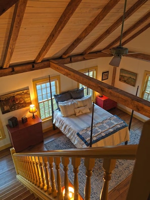Une chambre avec un plafond en pente, un lit recouvert dâune courtepointe, une table de chevet, une commode et une fenĂȘtre.