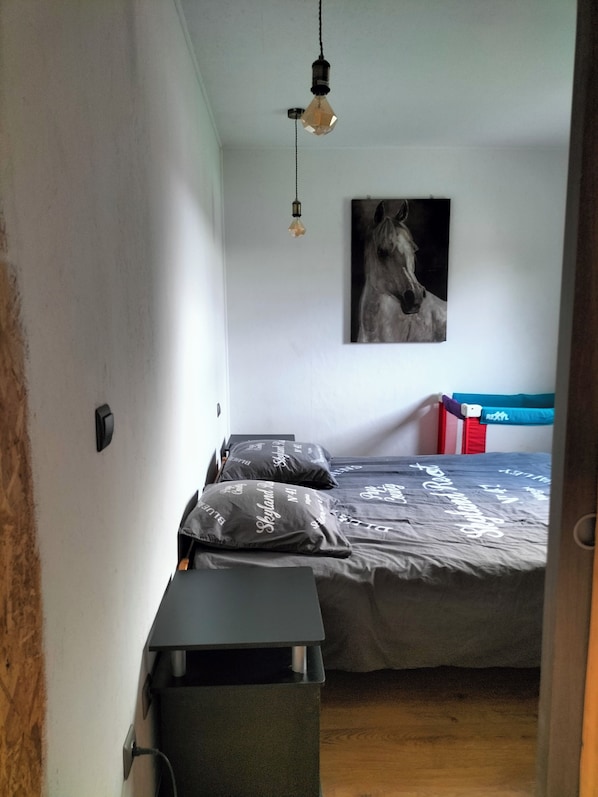 A bedroom with a bed, pillows, a hanging light fixture, and a wall-mounted painting.