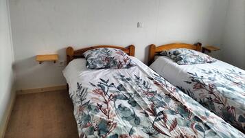 Een kamer met twee éénpersoonsbedden, houten hoofdborden, nachtkastjes en een effen witte muur.