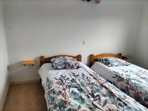 A room with two single beds, wooden headboards, bedside tables, and a plain white wall.