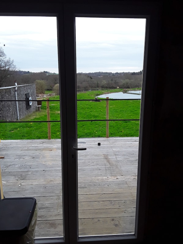 A view through a door of a wooden deck leading to a grassy area with a pond and a stone wall.