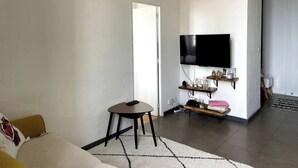 Ein Wohnzimmer mit einer Couch, einem kleinen Tisch, einem an der Wand befestigten Fernseher und einer Tür zu einem anderen Raum.