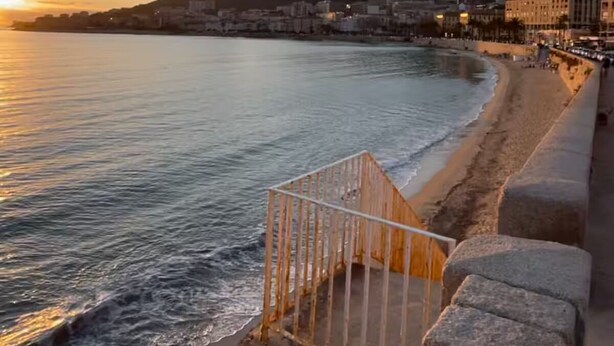 Eine Küstenstadt mit Strand, einer Steinmauer am Meer und Gebäuden im Hintergrund.