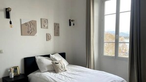 Ein Schlafzimmer mit Bett, Nachttisch, Wandbild und einem Fenster mit Blick.