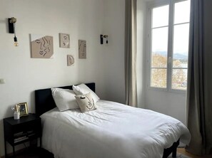 Ein Schlafzimmer mit Bett, Nachttisch, Wandbild und einem Fenster mit Blick.