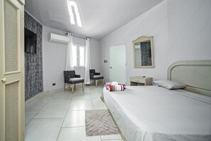 Ein Schlafzimmer mit einem Bett, einem Sessel, einem kleinen Tisch, einem Spiegel und einer Tür.