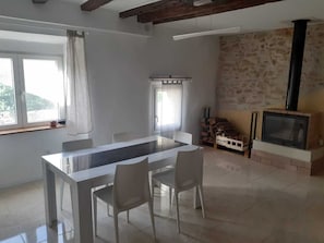 Eine moderne Küche mit einer zentralen Kochinsel, weißen Stühlen, einem Esstisch, einem Kamin und einem Fenster mit Vorhängen.