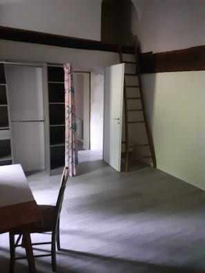 Ein Zimmer mit Tisch, Stühlen, einer Leiter und einer Tür zu einem anderen Raum.