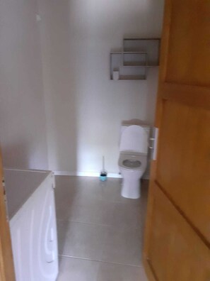 Ein schmaler Flur führt zu einem Badezimmer mit Toilette, Bidet und einem kleinen Regal über der Toilette.