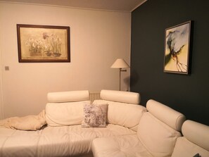 A room with a white sofa, a lamp, and two framed artworks on the wall.