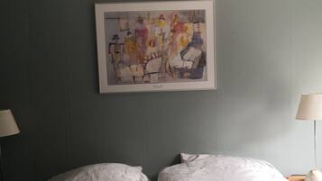 A room with a bed, two bedside lamps, and a framed abstract painting on the wall.
