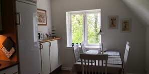 A kitchen with a dining table and chairs, a window with a view of trees, and a refrigerator.