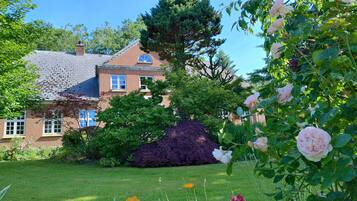 A brick house with a large tree in the yard, surrounded by greenery and flowers.
