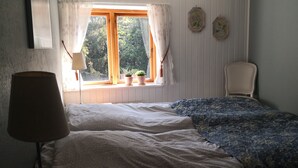 Une chambre avec un lit simple, une fenêtre avec des rideaux, une chaise et deux décorations florales fixées au mur.