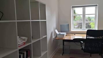 A room with a desk, chair, computer, bookshelf, and window with a view.