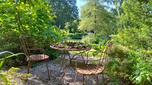 Een tuin met twee metalen stoelen en een tafel, omgeven door groen en een vijver.