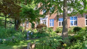Een tuin met een bakstenen gebouw, stenen sculpturen en weelderige begroeiing.