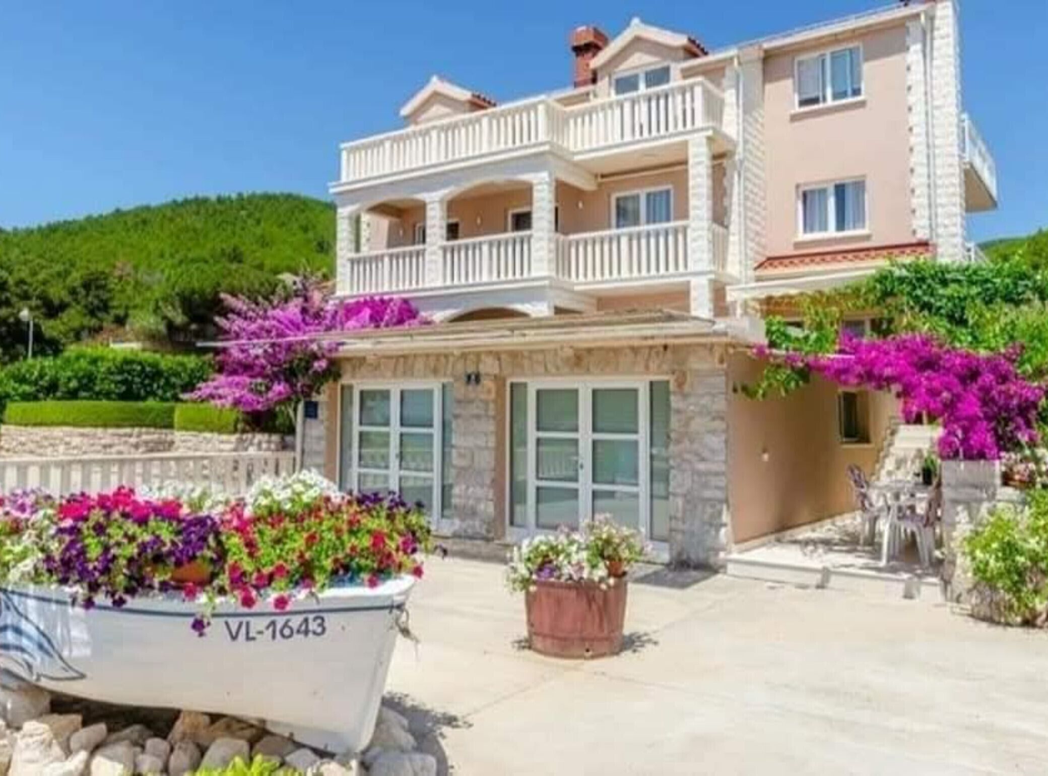 A multi-story building with balconies, stone facade, and flower beds.