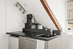 Eine Küche mit schwarzem Arbeitsplatz, Edelstahlgeräten, einer Kaffeemaschine und einem Fenster mit Jalousien.