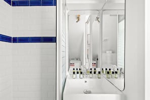 Ein Badezimmer mit weißen Fliesen, einem Spiegel, einem Waschbecken und Toilettenartikeln.
