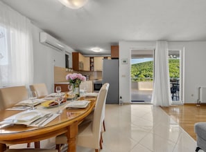 A dining area with a table set for four, a kitchen in the background, and a balcony with a view of greenery. - Three Bedroom Holiday Home with Private Pool and Terrace (Šibenik)