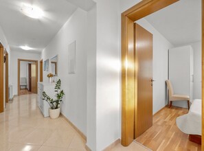 A hallway with a wooden door, a potted plant, a chair, and a bed in the adjacent room. - Three Bedroom Holiday Home with Private Pool and Terrace (Šibenik)