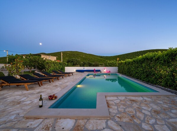 A swimming pool with lounge chairs, a bottle of wine, and fruit on the side. - Three Bedroom Holiday Home with Private Pool and Terrace (Šibenik)
