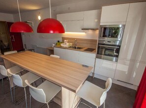 Eine moderne Küche mit einer Holztresle, weißen Schränken, Edelstahlgeräten und roten Pendelleuchten.